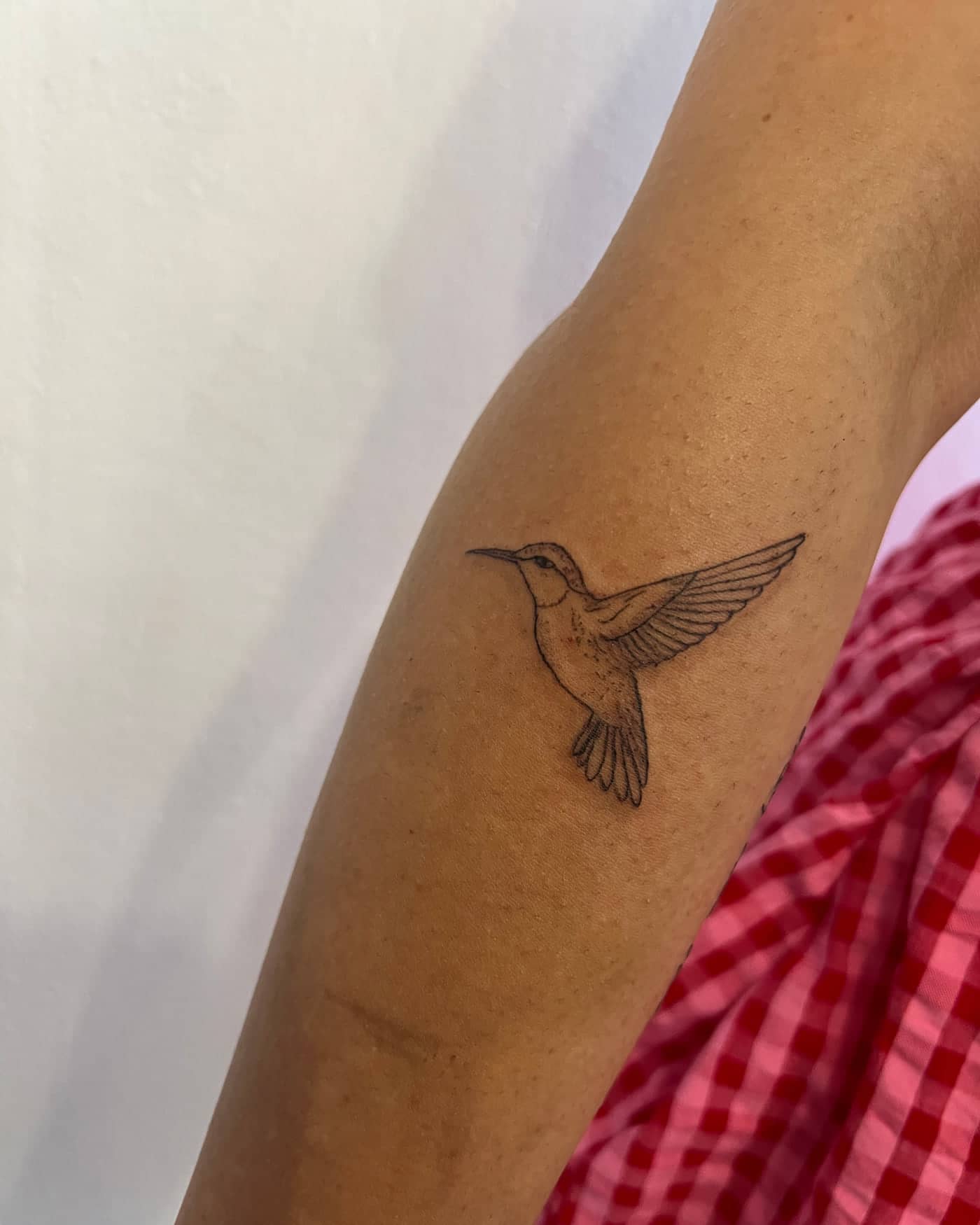 Fine line hummingbird tattoo in flight on the arm